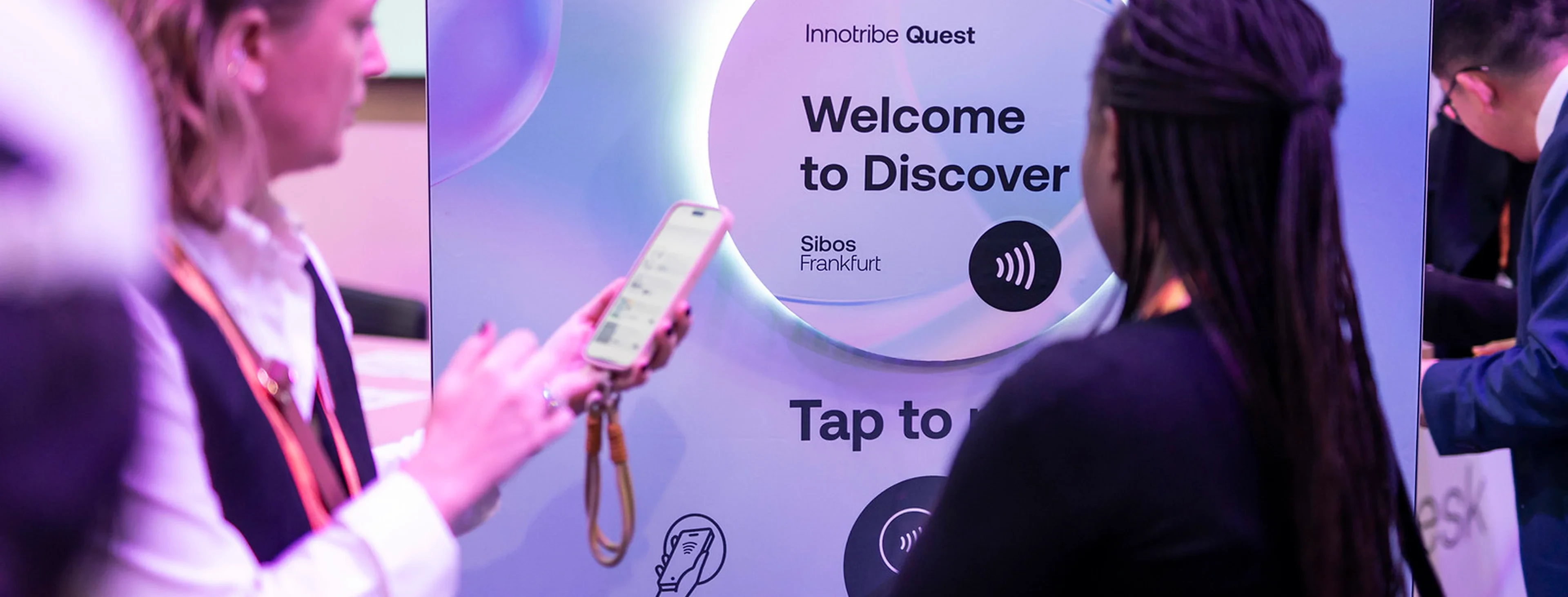 An attendee holding a phone to the Innotribe Quest NFC totem at Sibos Frankfurt, under the words Welcome to Discover