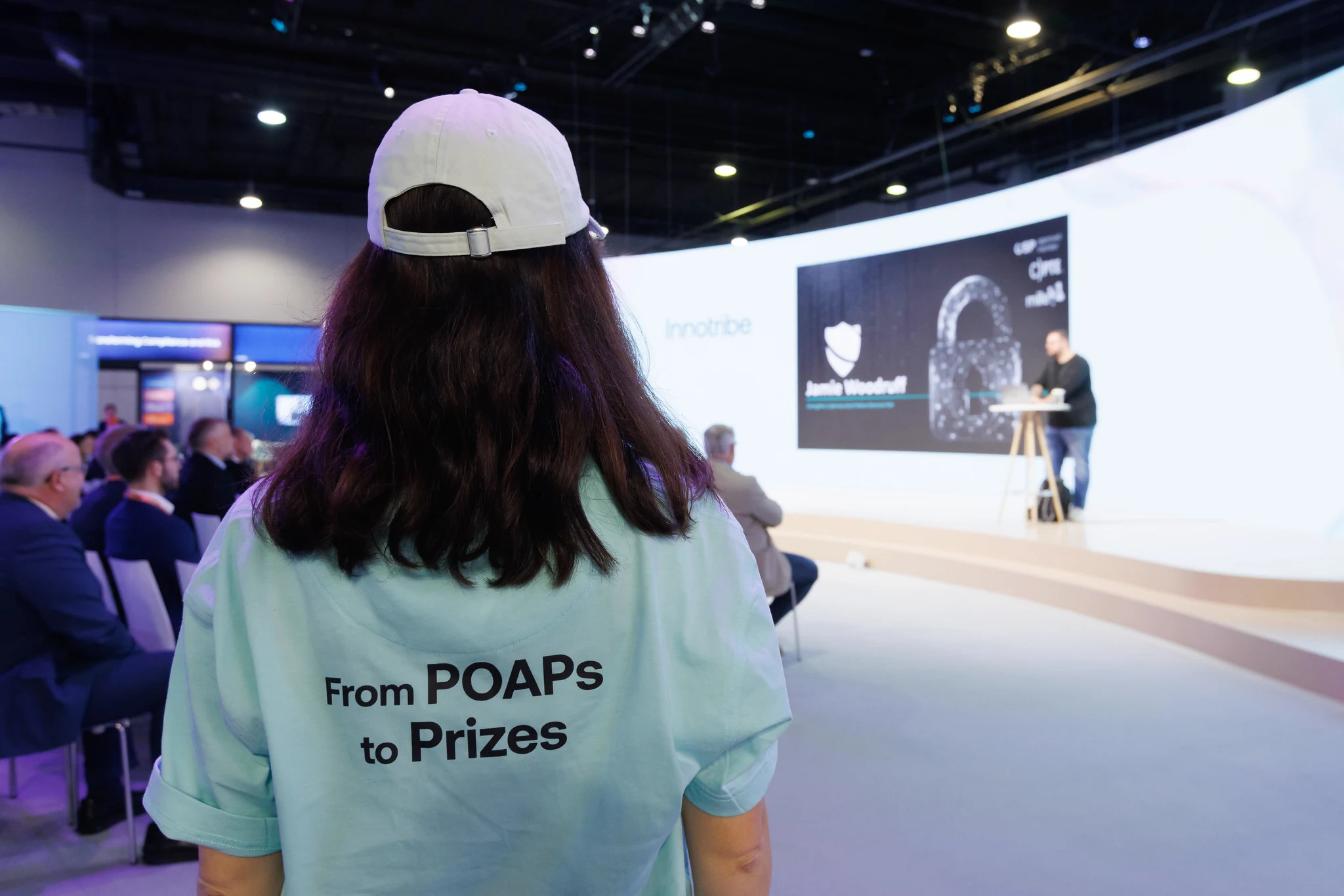 A Sibos attendee in a Quest t-shirt reading From POAPs to Prizes, watching a session in the Innotribe theatre